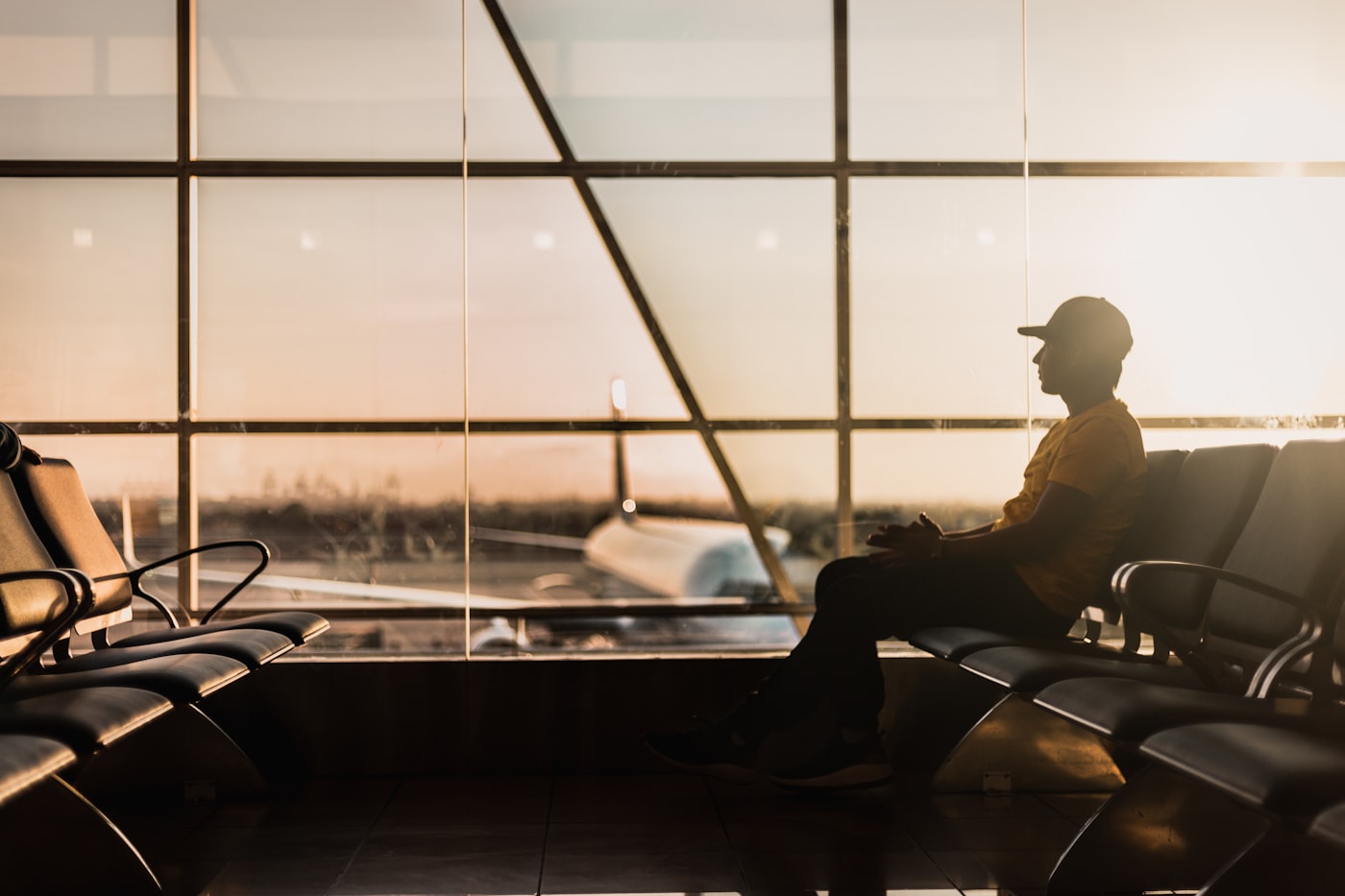 A young student waits at the departure gate at sunset, ready to fly abroad